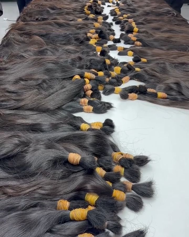 Various bundles of raw human hair sorted by length and color at a hair extension manufacturer's facility